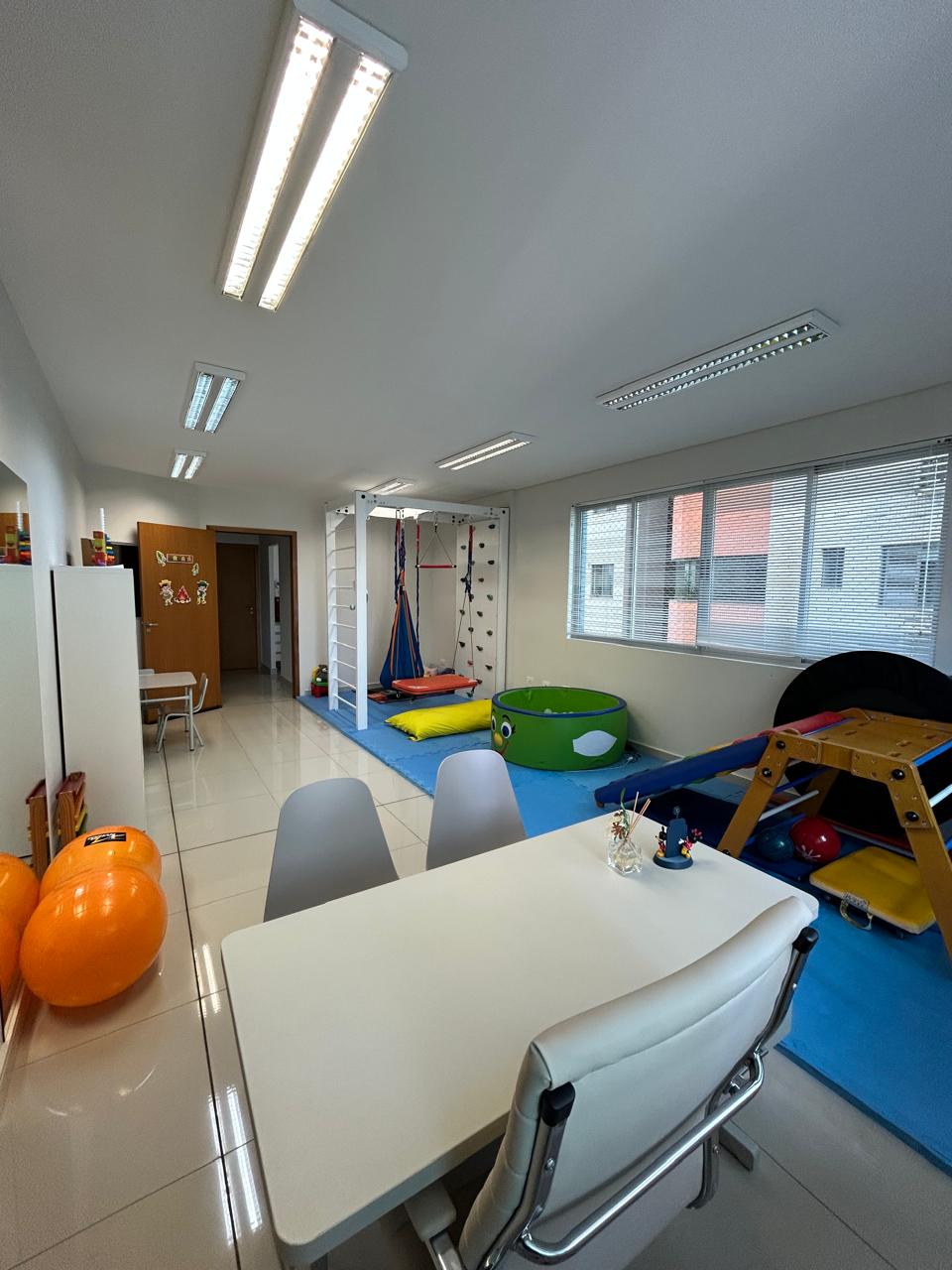 Sala ampla de integração sensorial com balanços, escalada e materiais terapêuticos